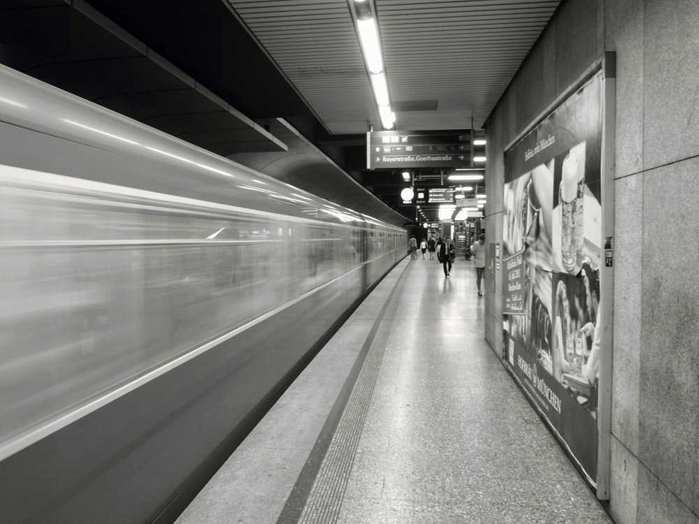 Person waiting in a grey subway station with few people while train leaves