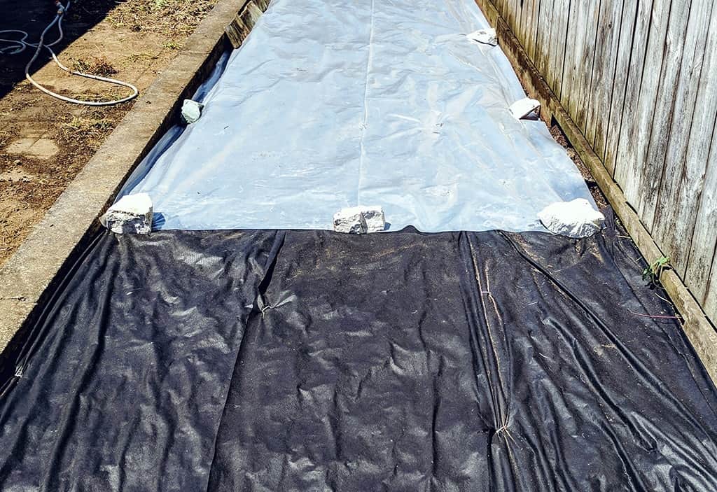 strip of garden half covered with a black weedmat and half with atransparent polyurethane